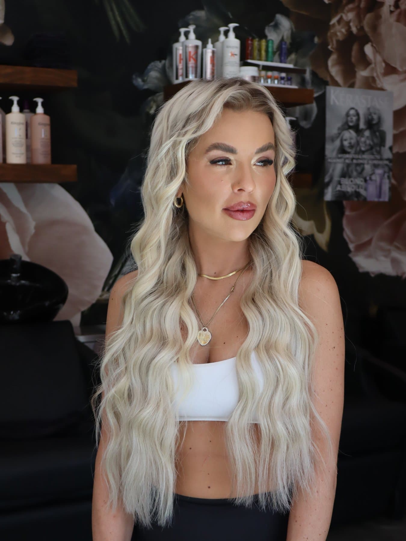 Bloom Salon ATX client with icy blonde extensions in front of the Kérastase shelf